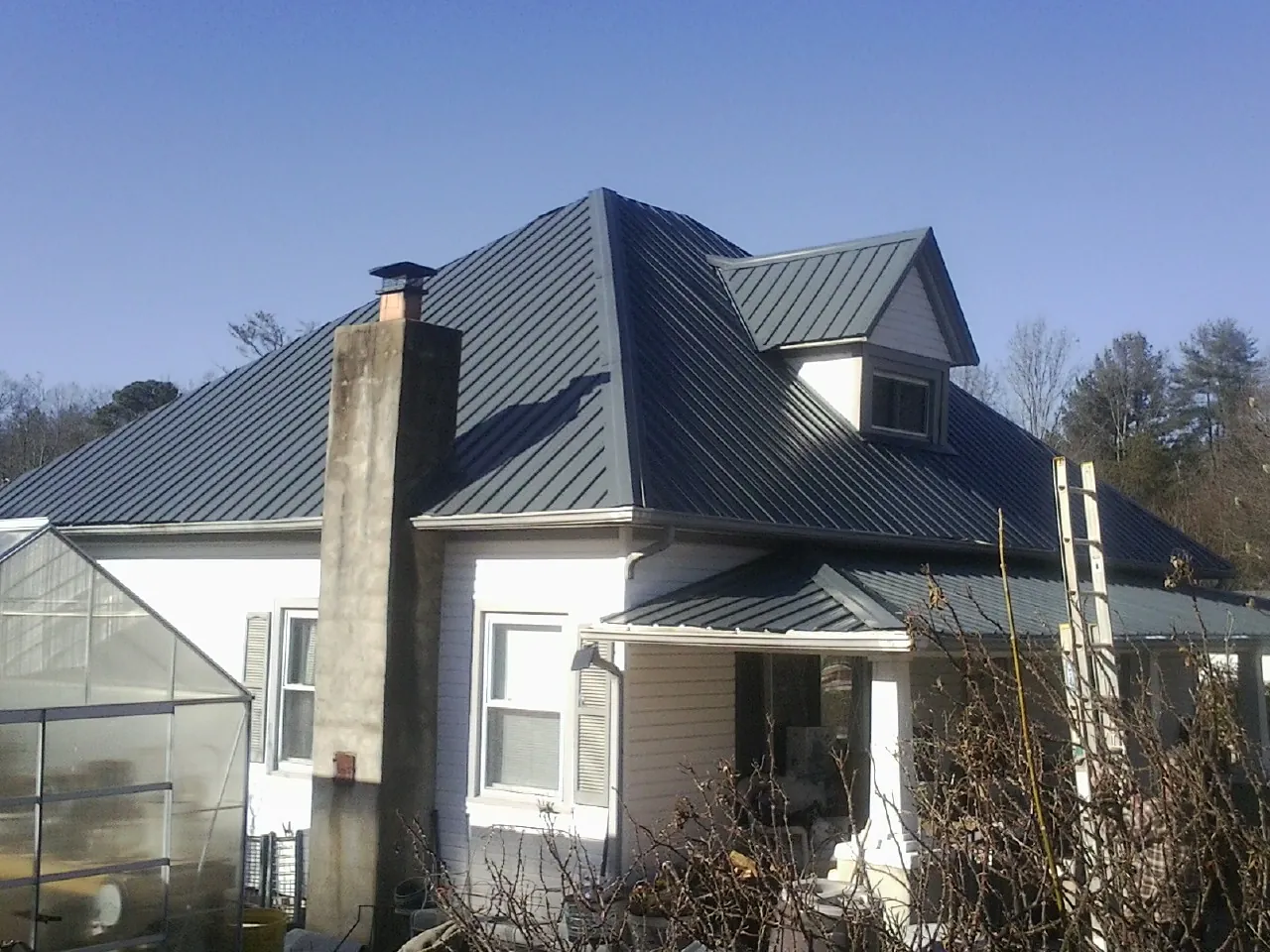 Dark blue standing seam metal roof on a white farmhouse with dormer — Slate & Tile Roof Repair by Roofing Brothers in Pinehurst