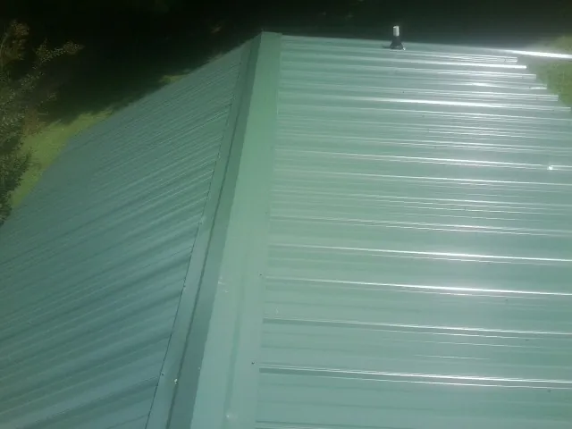 New green metal panels meeting at the ridge of a roof — Flat Roof Repair work by our crew in Pinehurst